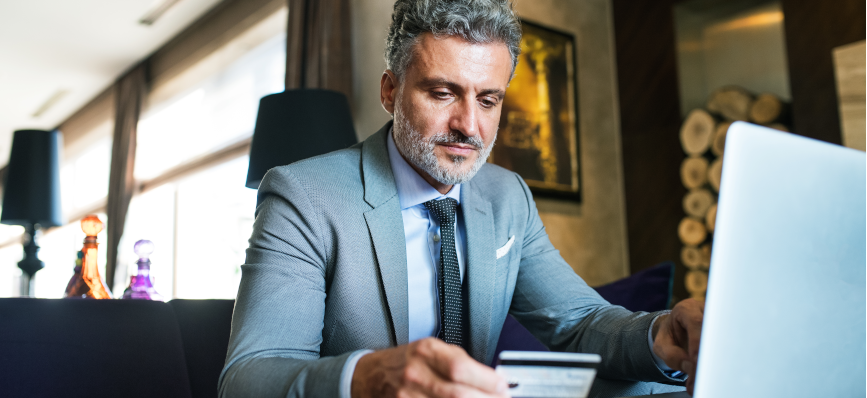 This image shows a man sitting at a computer with his bank card in his hand.