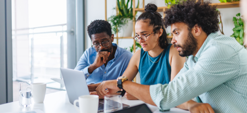 This image shows three people sat at a table looking at a computer screen. 