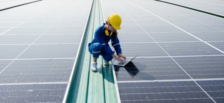 A worker using a laptop on a roof covered with solar panels