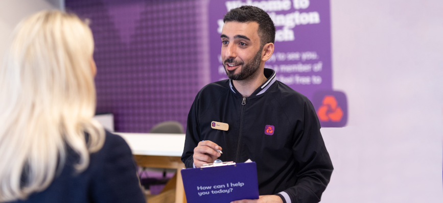 NatWest colleague at NatWest branch, smiling at customer who has her back to the camera