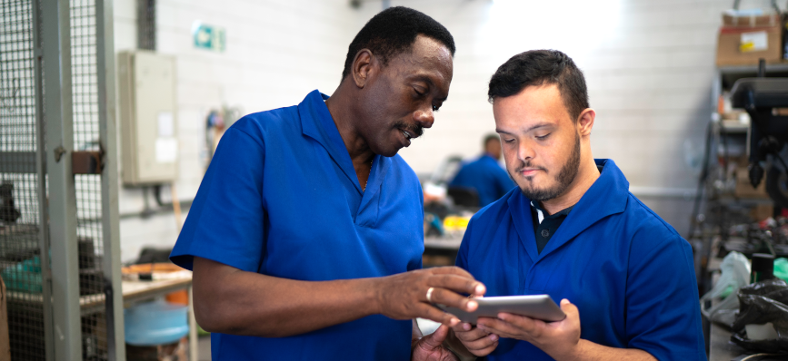 This image shows two workers in a factory looking at a tablet device.