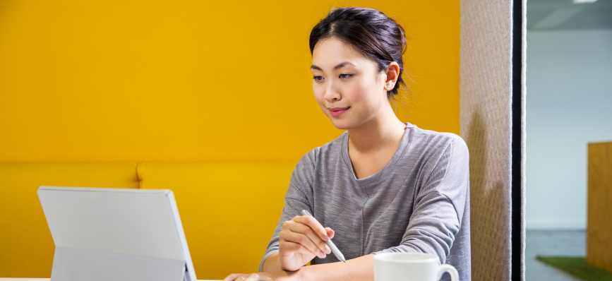 Shot shows a woman sitting at a desk looking at a tablet computer