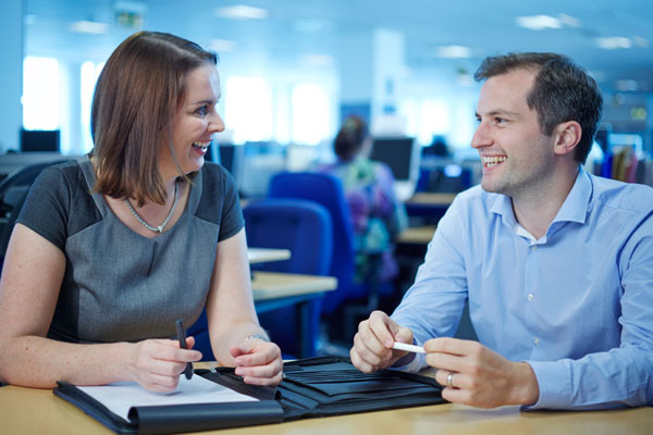 Woman and man talking at a table in an open plan office
