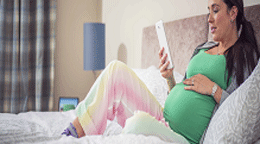 Pregnant woman sitting on a bed with a tablet